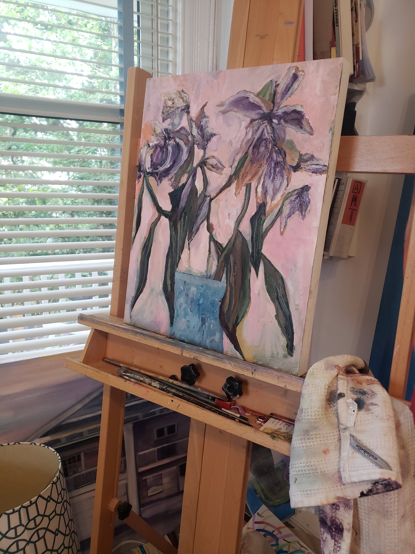 A painting of flowers on a shelf with books and art supplies.
