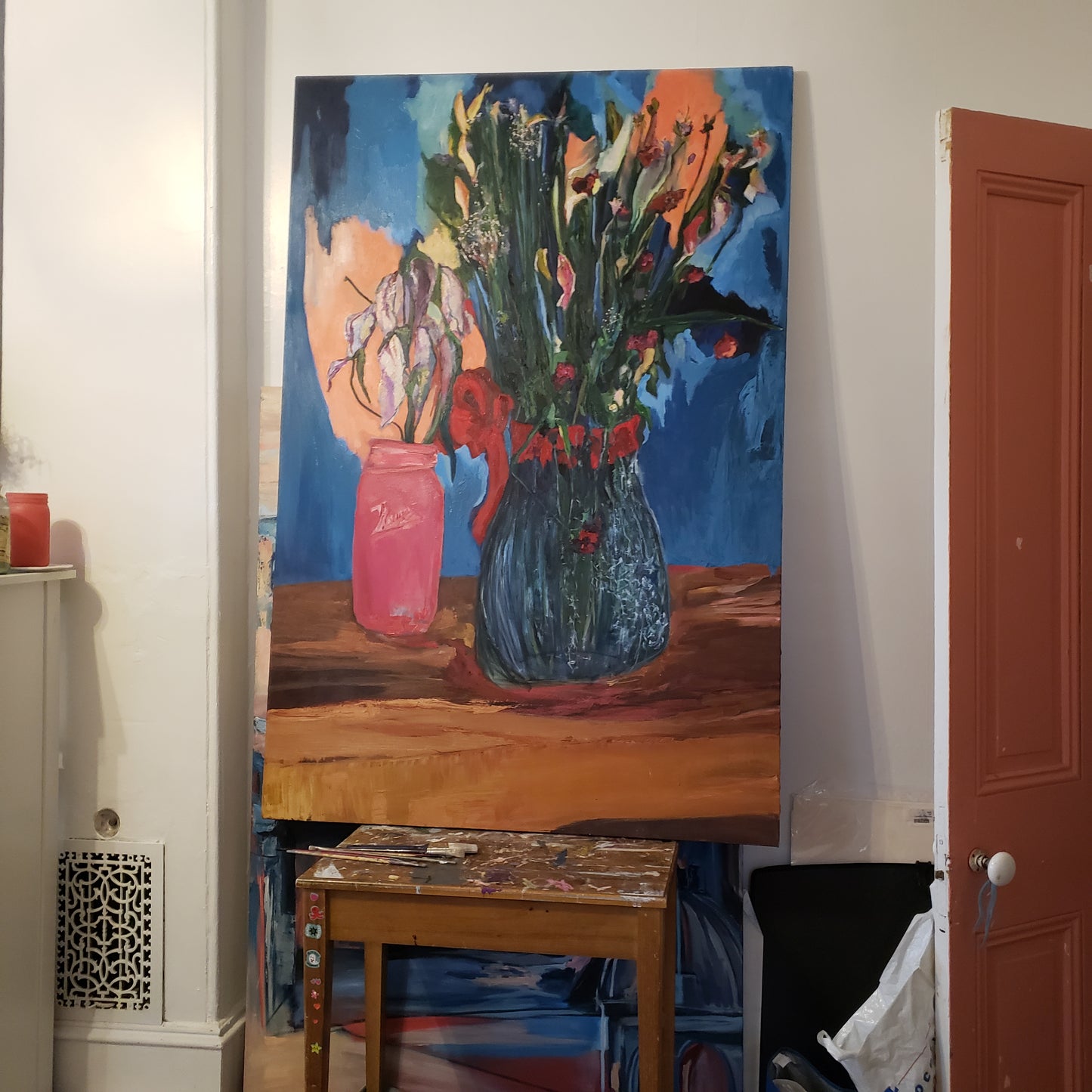 Colorful oil painting of flowers on a wall above a shelf with books and decor.